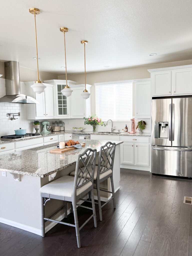 white kitchen cabinets with brass hardware, tan granite counters, large island with pendant lights and range