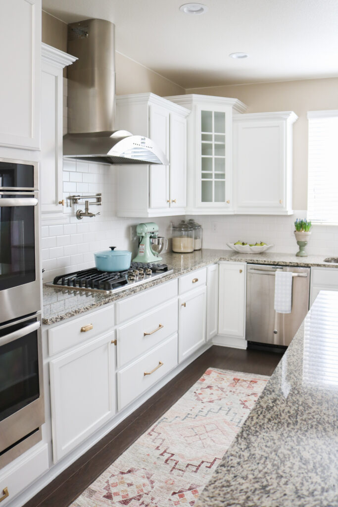white kitchen cabinets with brass hardware, tan granite counters with double ovens, range and hood and large island