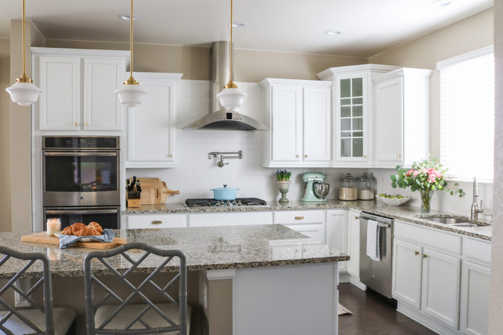 white kitchen cabinets with brass hardware, tan granite counters, large island and range